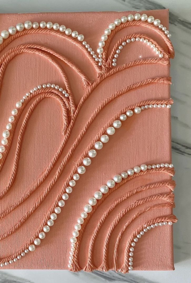 an art work with pearls and beads on pink paper, sitting on a marble surface