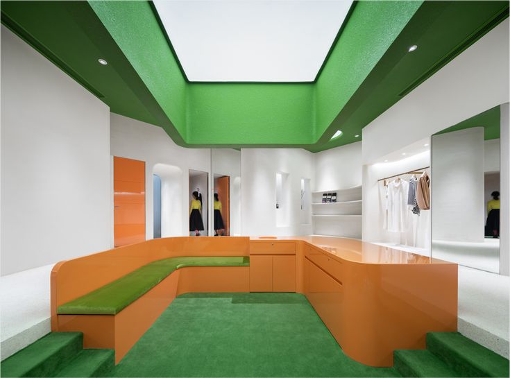 a room with green and orange carpeting, white walls, and an l shaped bench