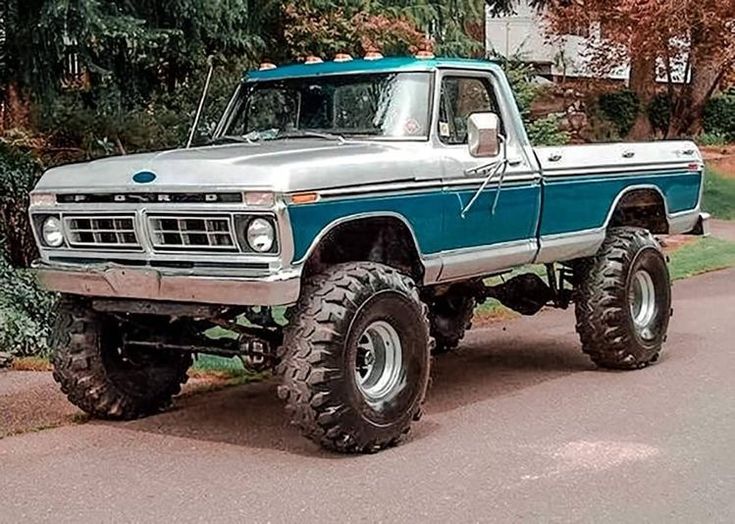 a blue and silver truck parked on the side of a road next to some trees