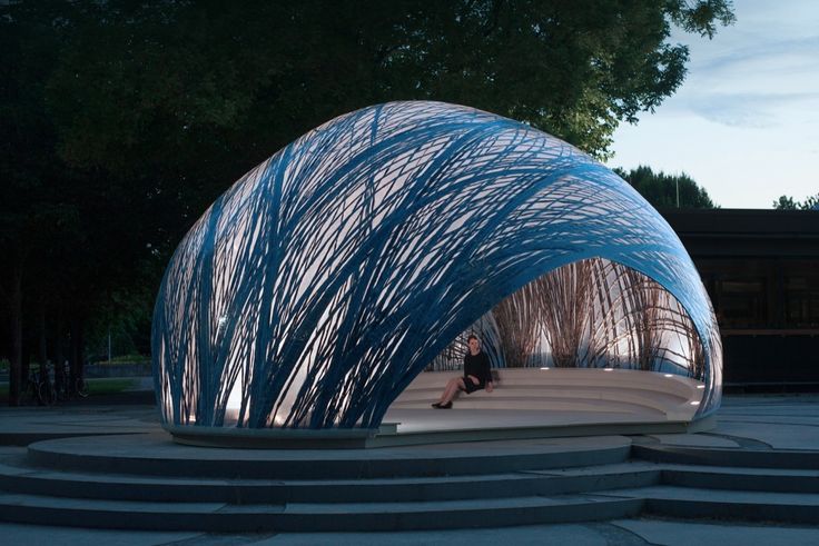 a person sitting on a bench in front of a sculpture that looks like an umbrella