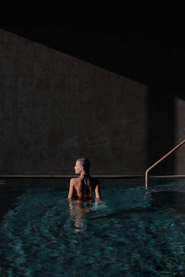 a woman sitting in the middle of a swimming pool with her back turned to the camera