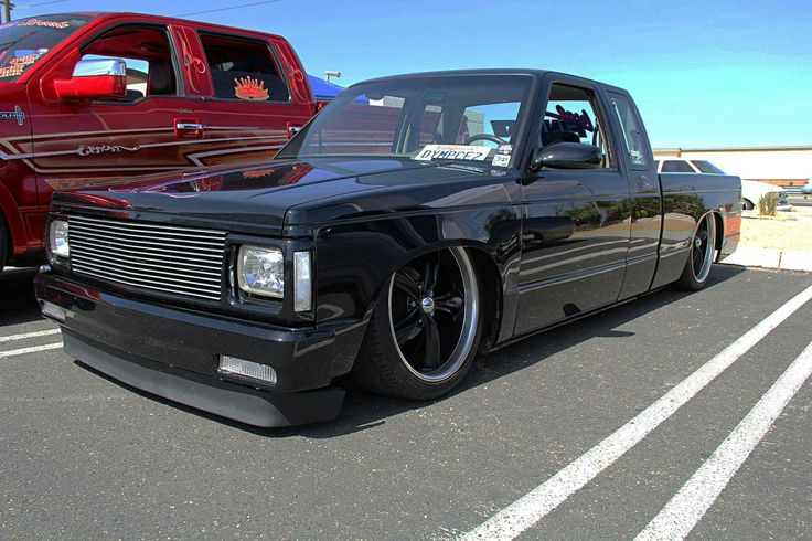 a black truck parked in a parking lot next to another red car and other vehicles