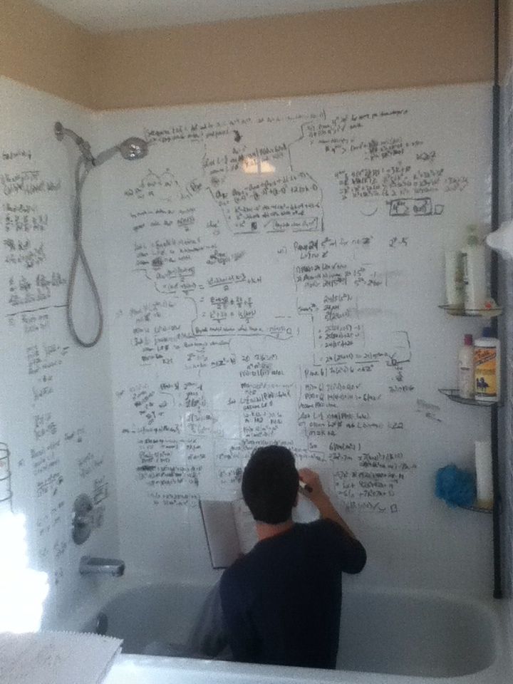 a man writing on a whiteboard in a bathtub next to a shower head