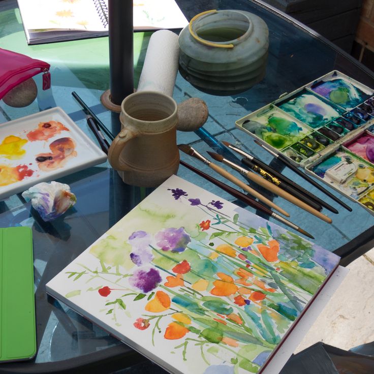 a table with art supplies and watercolors sitting on it's glass top