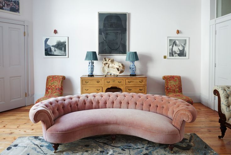 a pink couch sitting on top of a wooden floor next to two blue and white vases