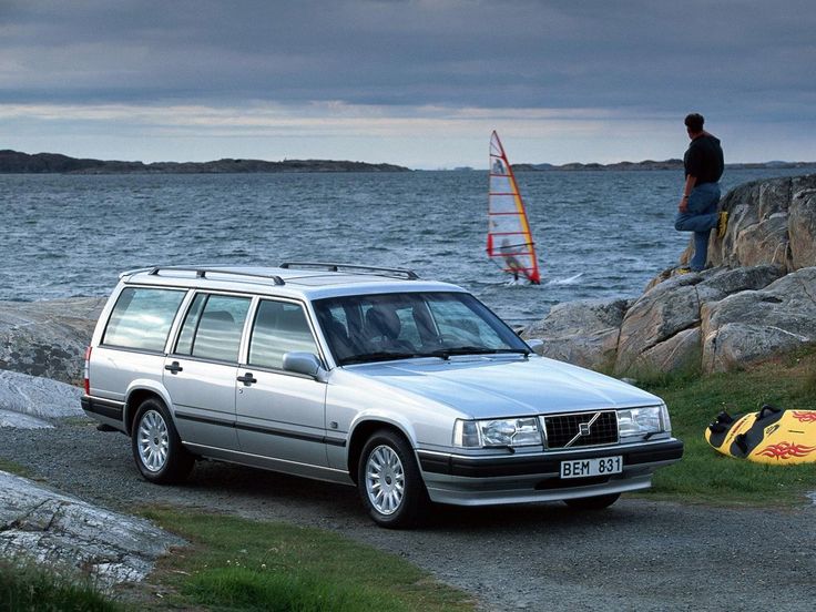 an suv parked next to the water with a man standing on rocks in the background