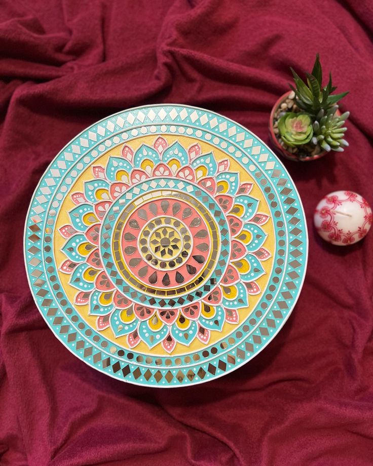 a colorful plate sitting on top of a red cloth next to an orange pineapple