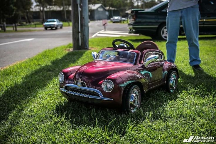 a toy car sitting on top of a lush green field next to a person standing in the grass