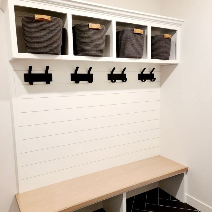 a white bench with baskets on it and some black hooks hanging from the back wall