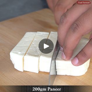 a person cutting cheese with a knife on top of a wooden table next to a video screen