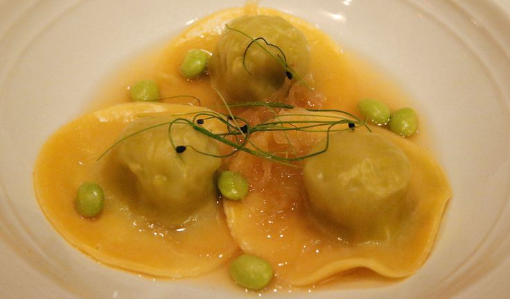 three ravioli with peas on a white plate, garnished with green olives