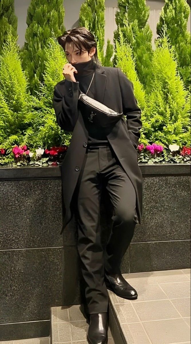 a man in a black suit and tie sitting on a ledge next to some plants