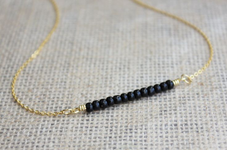 Minimalist Black Seed Bead Bar Necklace This delicate 16k gold layering necklace features a bar of black glass seed beads.  The jump rings and the lobster clasp are all 14k gold plated. The handmade necklace measures 17 1/2 inches in length. (Last photo is a reference of size.) View more of our handmade casual necklaces: https://www.etsy.com/shop/PeabodiesGlasshouse?section_id=17612340 Glass Bead Jewelry, Bead Bar Necklace, Boho Statement Necklace, Delicate Gold Necklace, Raw Gemstone Jewelry, Casual Necklaces, Bead Bar, Glass Beads Jewelry, Black Seed