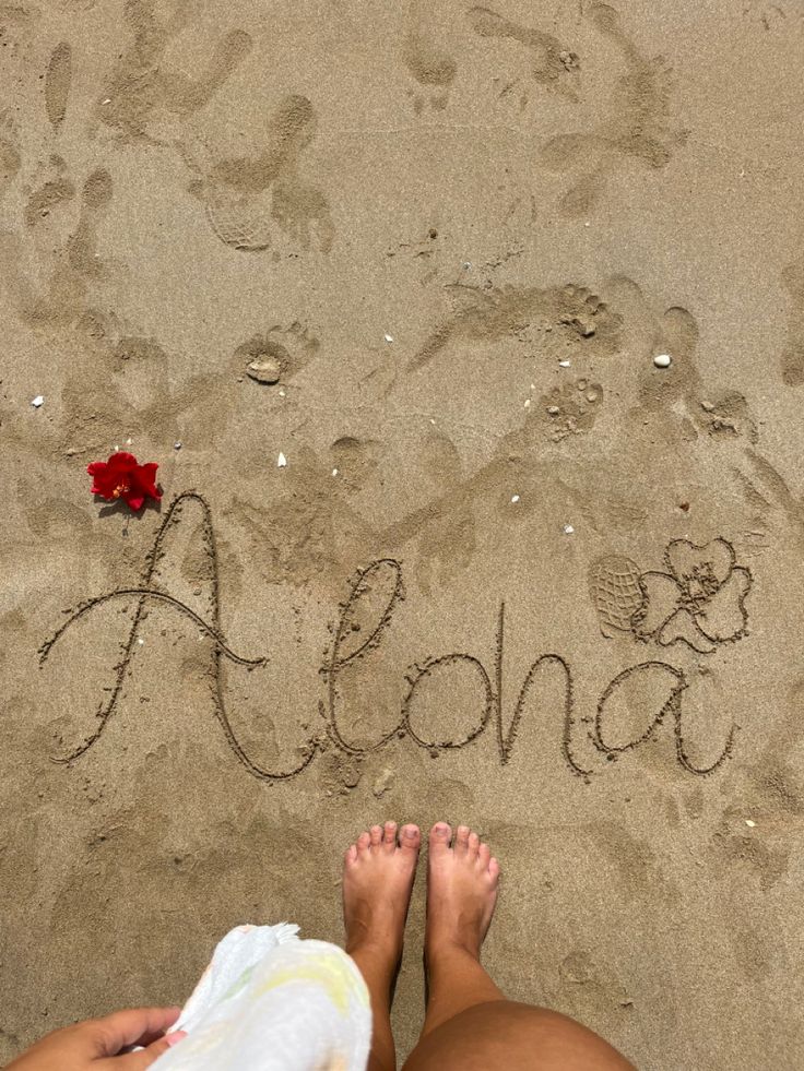 someone is writing aloha in the sand at the beach with their feet up