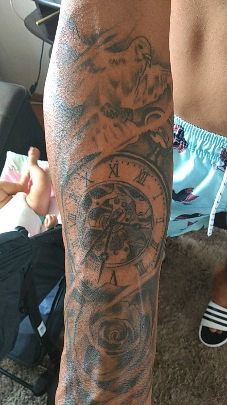 a man's arm with a clock tattoo on it, and his leg in the background