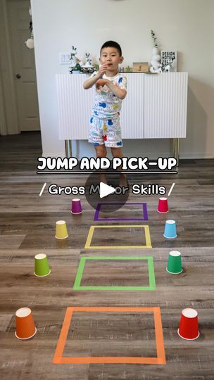 a young boy standing on top of a wooden floor next to colorful cups and cones