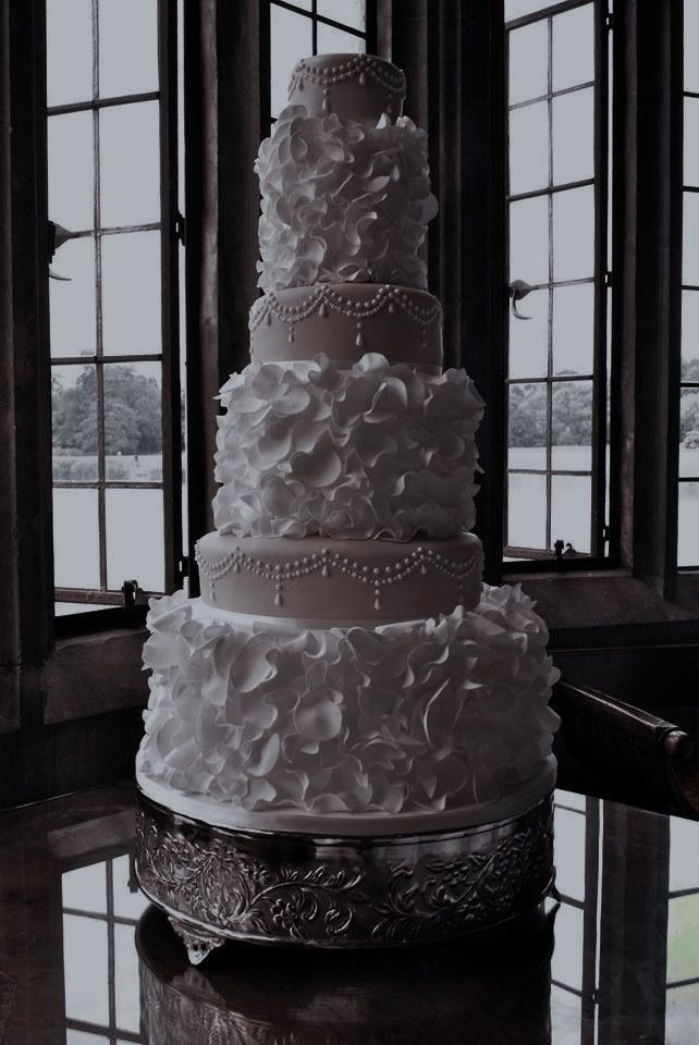 a large white wedding cake sitting on top of a table next to two windows with panes in the background