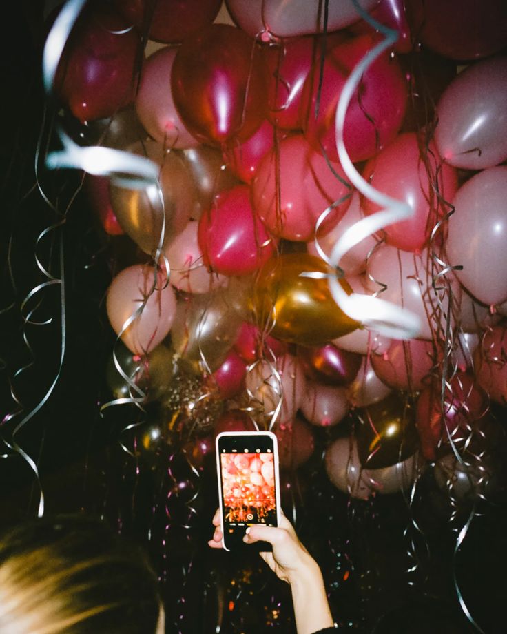 a woman taking a photo with her phone surrounded by balloons and streamers