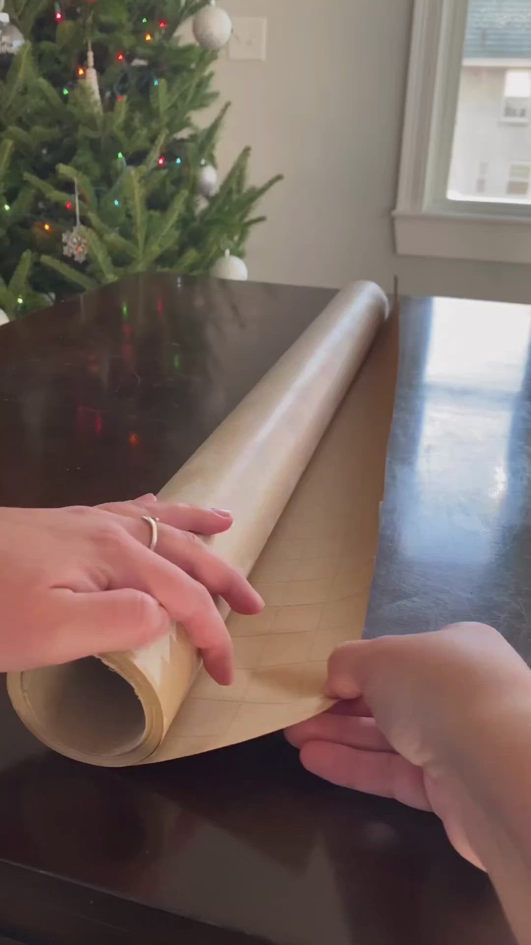 This may contain: someone wrapping up a christmas tree paper on top of a table next to a christmas tree