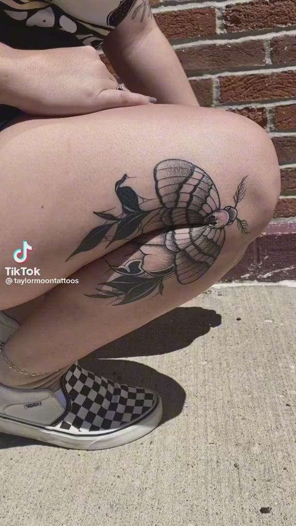 This may contain: a woman sitting on the ground with her legs crossed and tattoos on her leg,