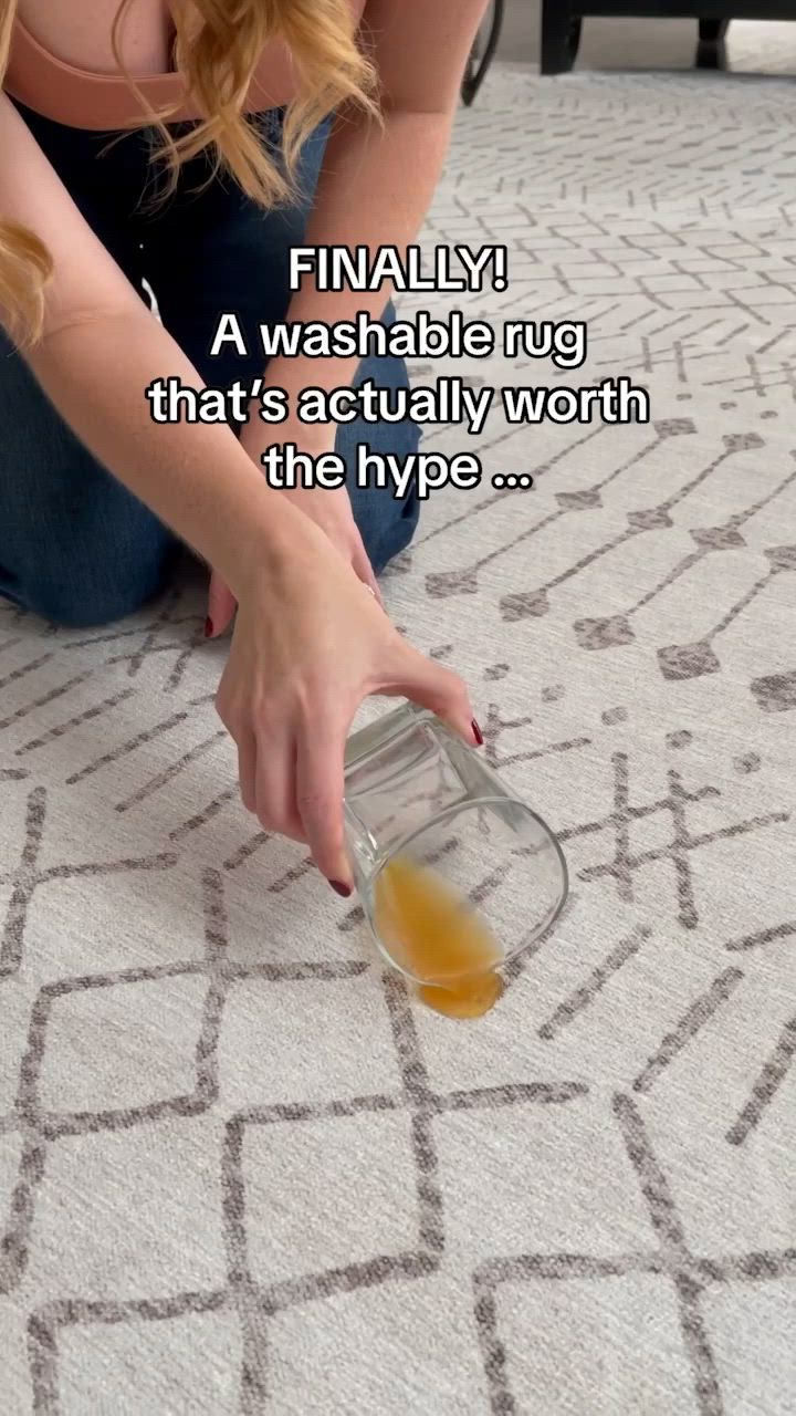 This may contain: a woman sitting on the floor with an empty glass bottle in her hand and a caption that reads, finally a washable rug that's actually worth the hyp?