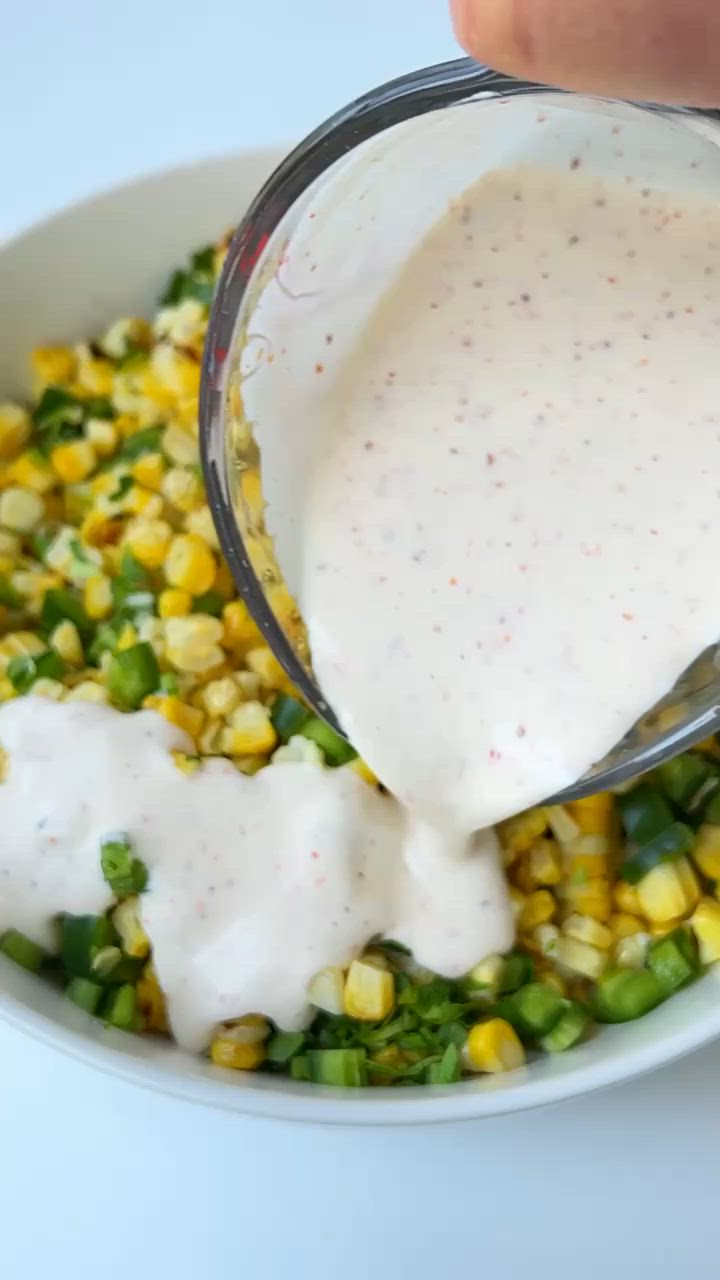 This may contain: a white bowl filled with corn salad next to a lemon wedge