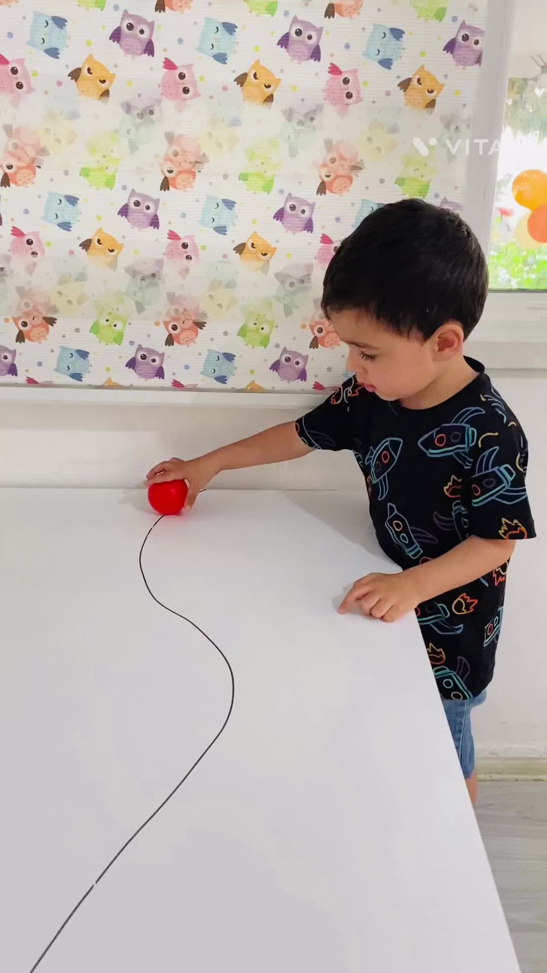 This may contain: a young boy playing with an apple on top of a white table in front of a colorful wall