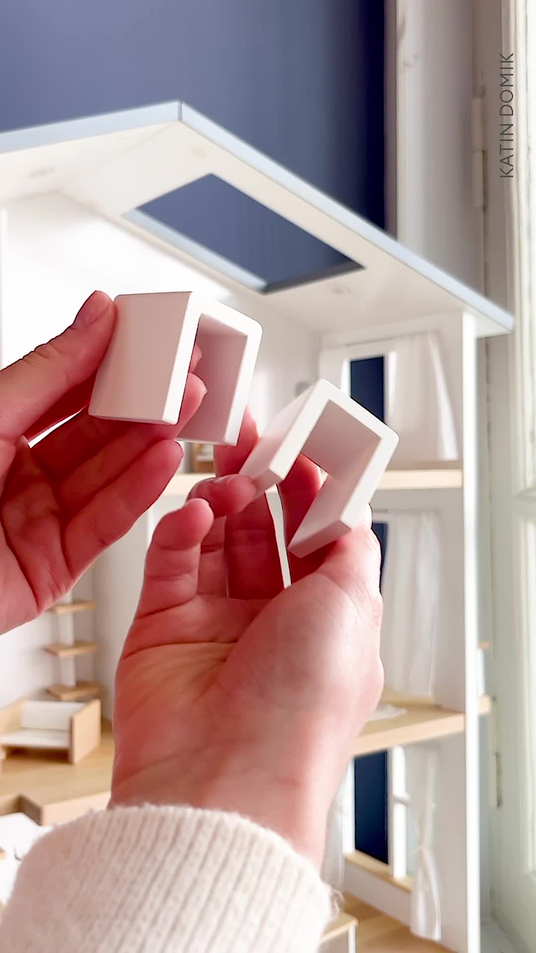 This may contain: a hand holding a magnifying glass in front of a doll house with shelves