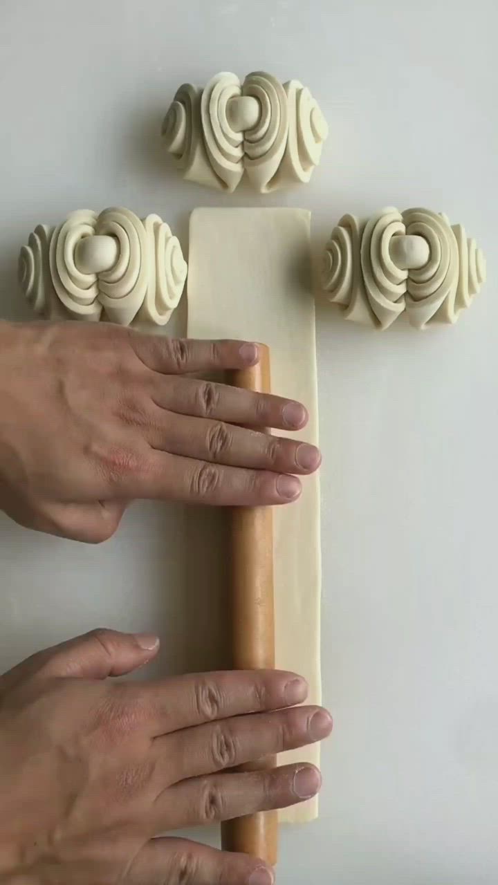 This may contain: two hands are holding a piece of wood with carved designs on it and the other hand is using a rolling pin