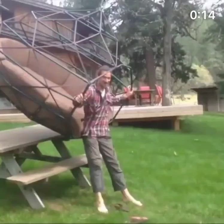 This may contain: a man standing next to a giant wooden object on top of a green grass covered field