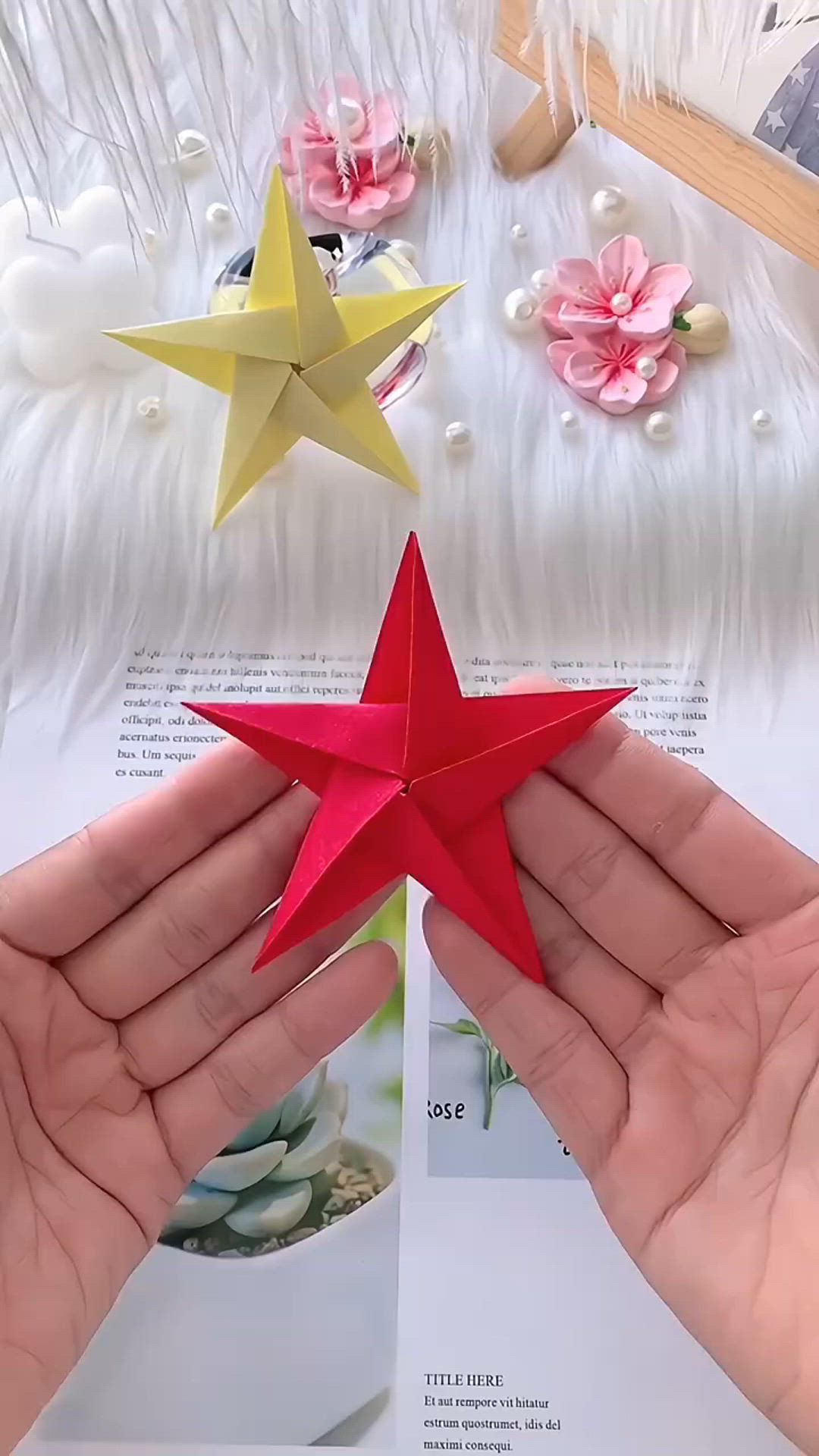 This may contain: two hands holding up a red and yellow origami star on top of a white table