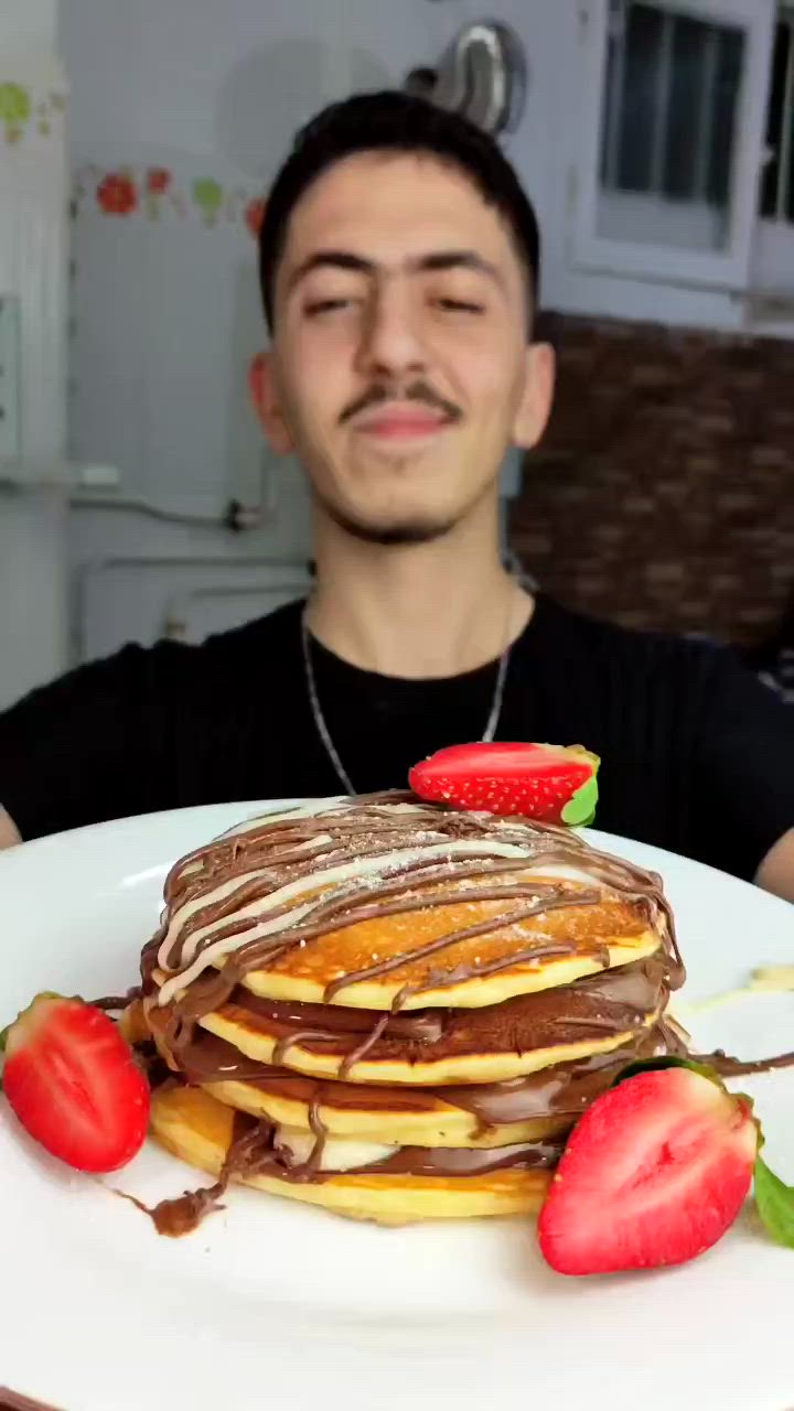 This may contain: a man is holding up a plate with pancakes and strawberries on it in front of him