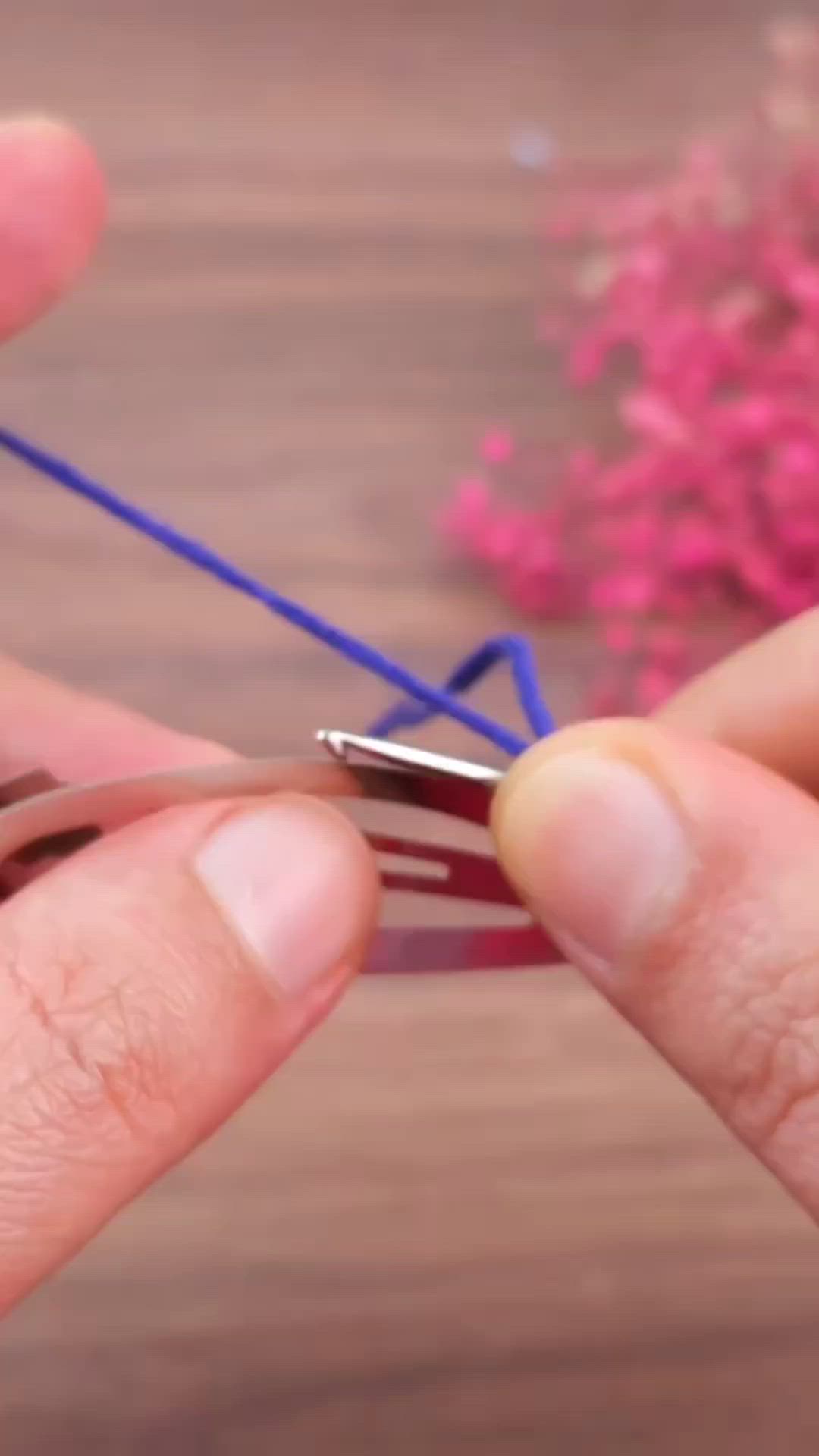 This may contain: two hands are holding scissors and stringing the ends of some blue wire with pink flowers in the background