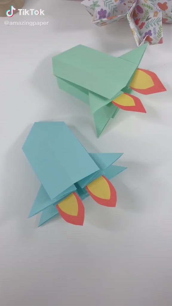 This may contain: two origami birds sitting on top of a table next to some paper flowers