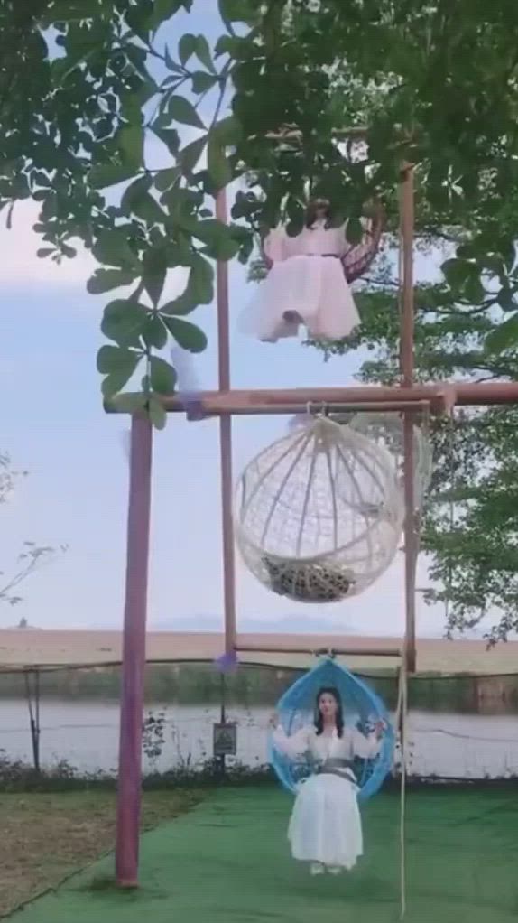 This may contain: a woman in a white dress standing under a tree next to a hammock