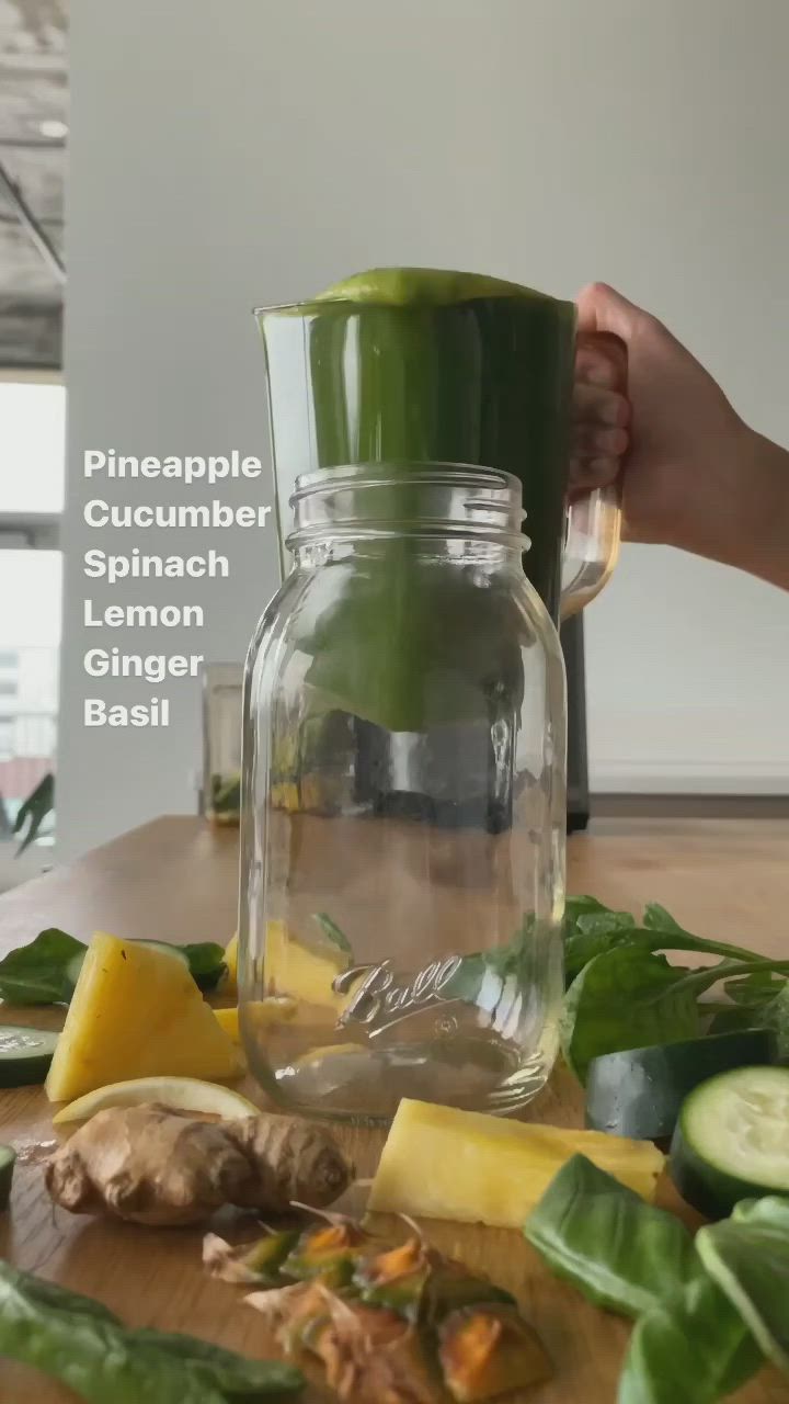 This may contain: a person is pouring green liquid into a jar with cucumber spinach lemon ginger basil