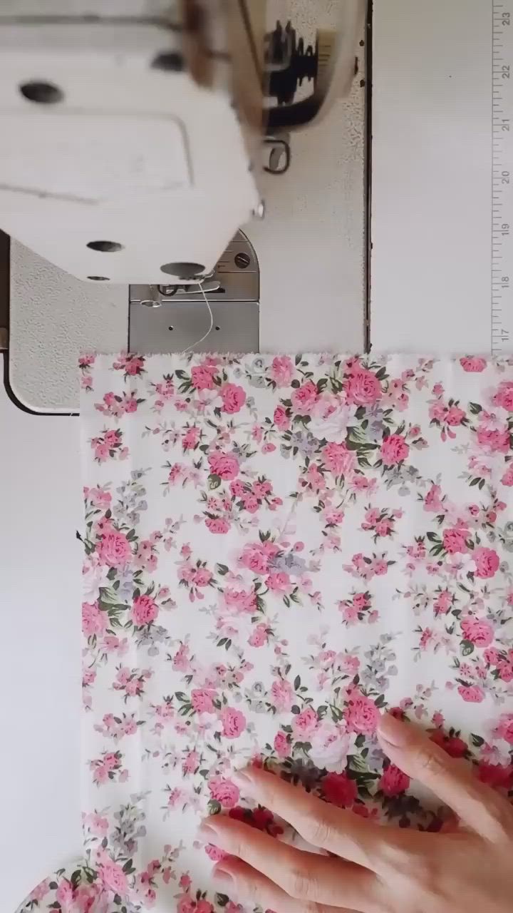 This may contain: a woman is using scissors to cut fabric with floral designs on the tablecloth and sewing machine behind her