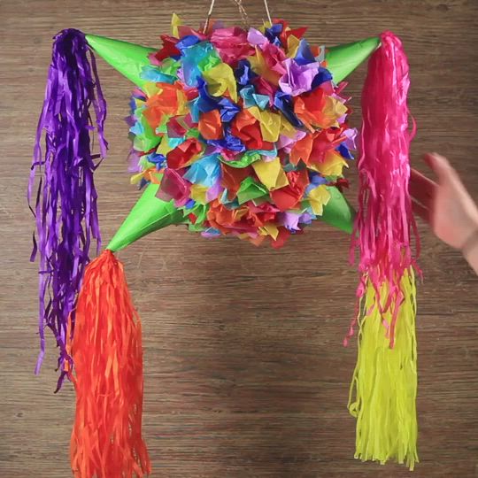 This may contain: a person is holding up a colorful pinata hanging from a string on the wall