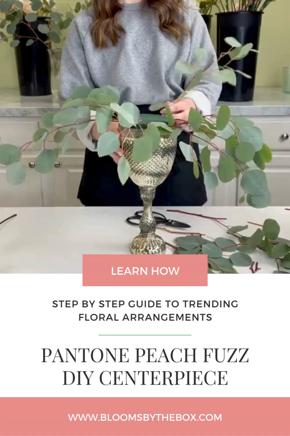 This may contain: a woman standing in front of a table with flowers and greenery on it, text overlay reads learn how step by step guide to trending floral arrangements