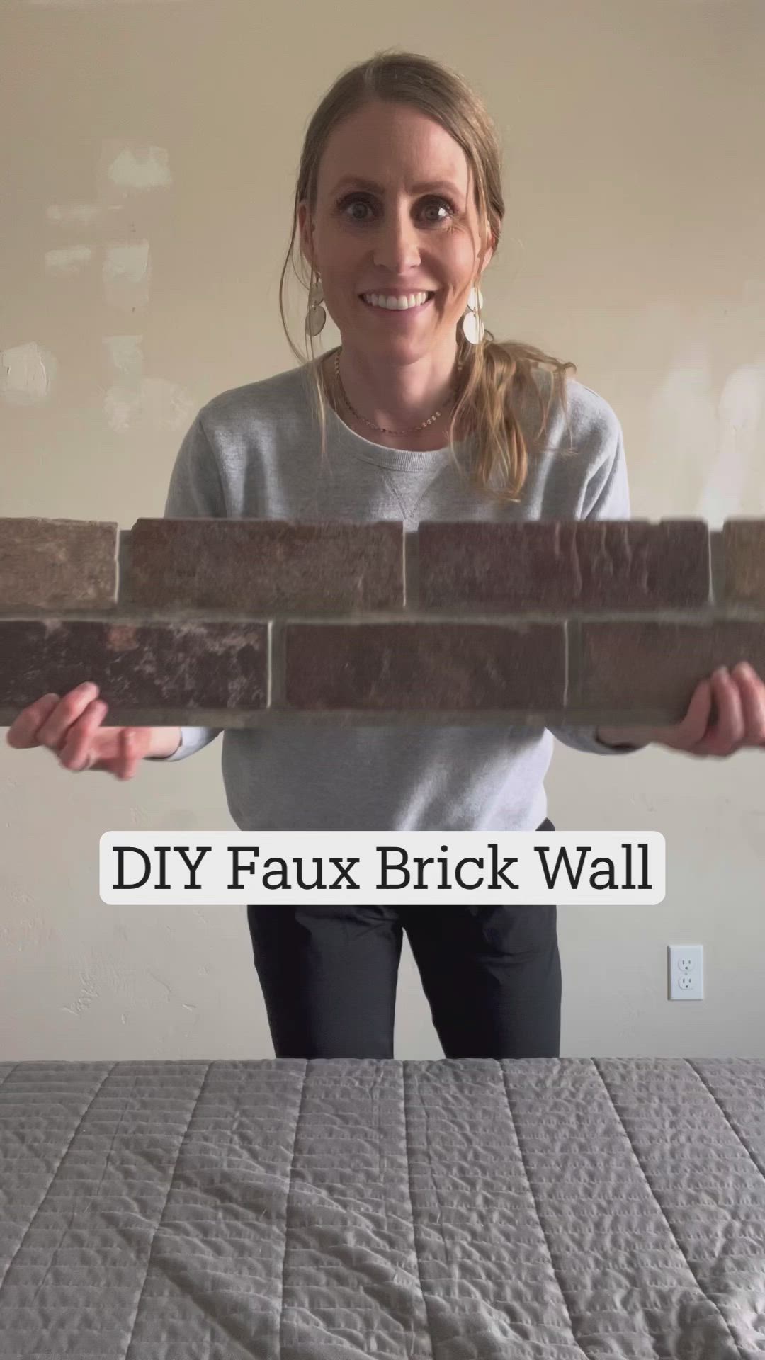 This may contain: a woman standing behind a brick wall with the words diy faux brick wall