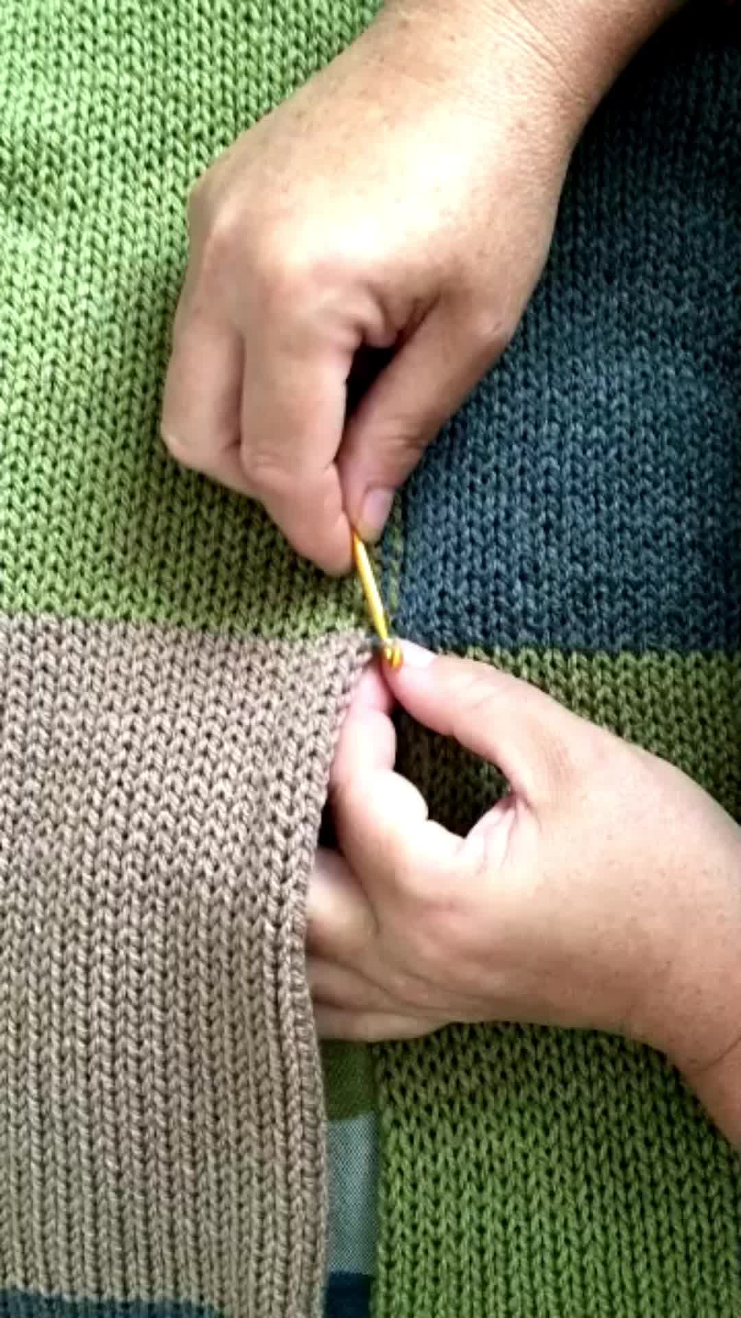 This may contain: a person is knitting on a green and blue striped knitted blanket with two hands