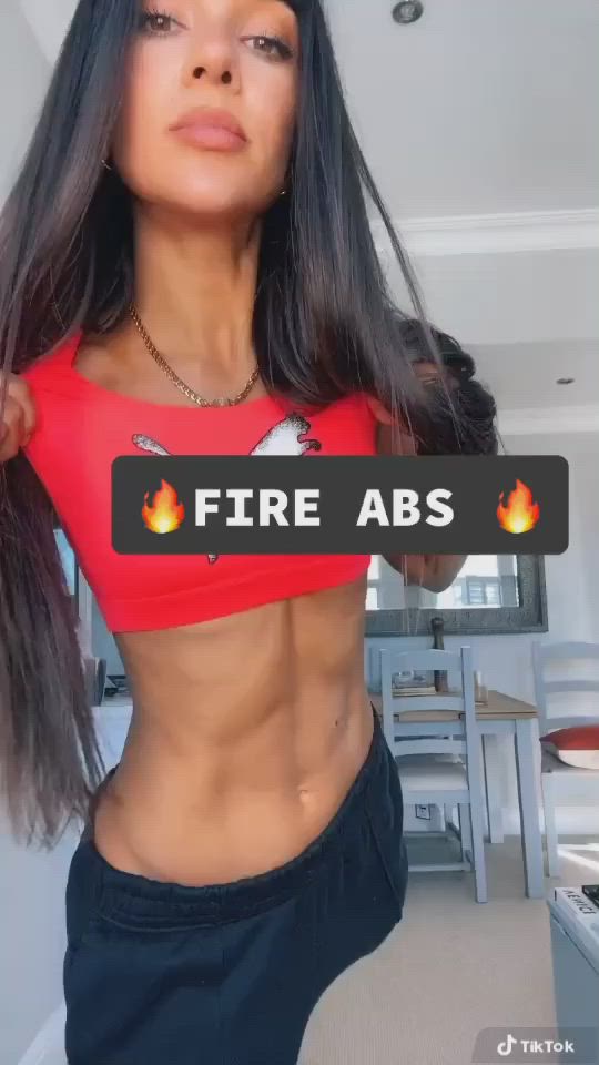 This may contain: a woman in red top and black pants with fire abs on her chest posing for the