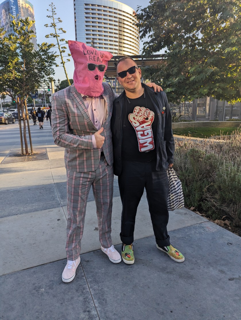 A photo of me with Chuck Tingle, who wears a pink bag over his head on which he has written 'Love is Real.'