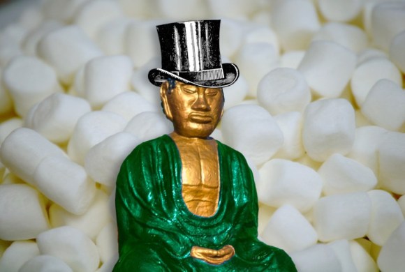 A serene, cross-legged, gilded Buddha statue; he is wearing a top-hat and posed on a field of white, fluffy marshmallows.