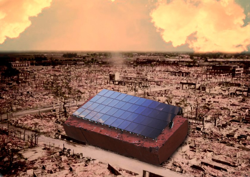 A firebombed cityscape under a smoky red sky. In the foreground is a gigantic brick, most of the length of a city block, with a set of solar panels atop it.