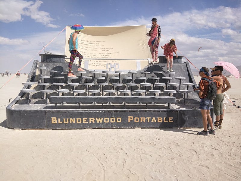 A giant typewriter sculpture at Burning Man, with several people admiring and climbing on it.