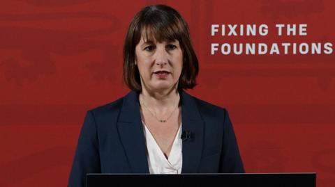 Rachel Reeves stands in front of a red wall at a press conference