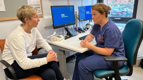 Laura Gelder-Robertson sitting at a desk speaking to a practitioner at Berkeley Place Surgery