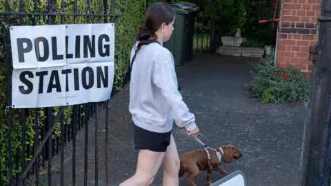 A young woman entering a polling station in the UK while walking her dog.