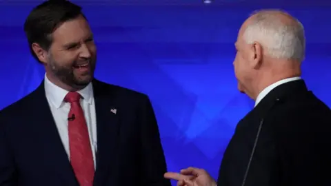 JD Vance smiles and Tim Walz gestures as they talk after the VP debate